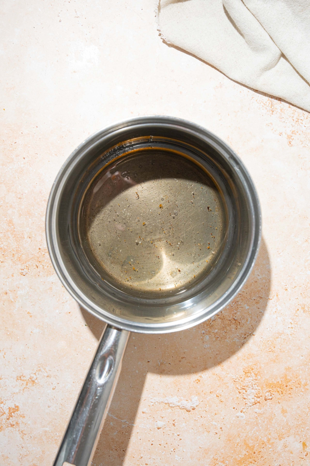 A saucepan with bacon grease, vinegar, water, and sugar. The saucepan is on a tan counter with a white cloth napkin.