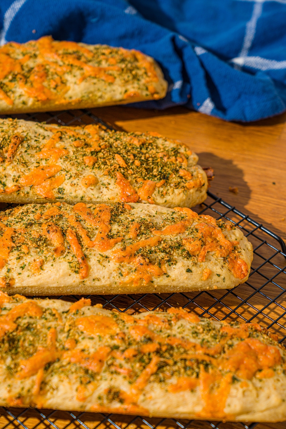 Half of three rolls of Italian herbs and cheese bread on a black wire rack. Behind that is half of another Italian herbs and cheese bread.