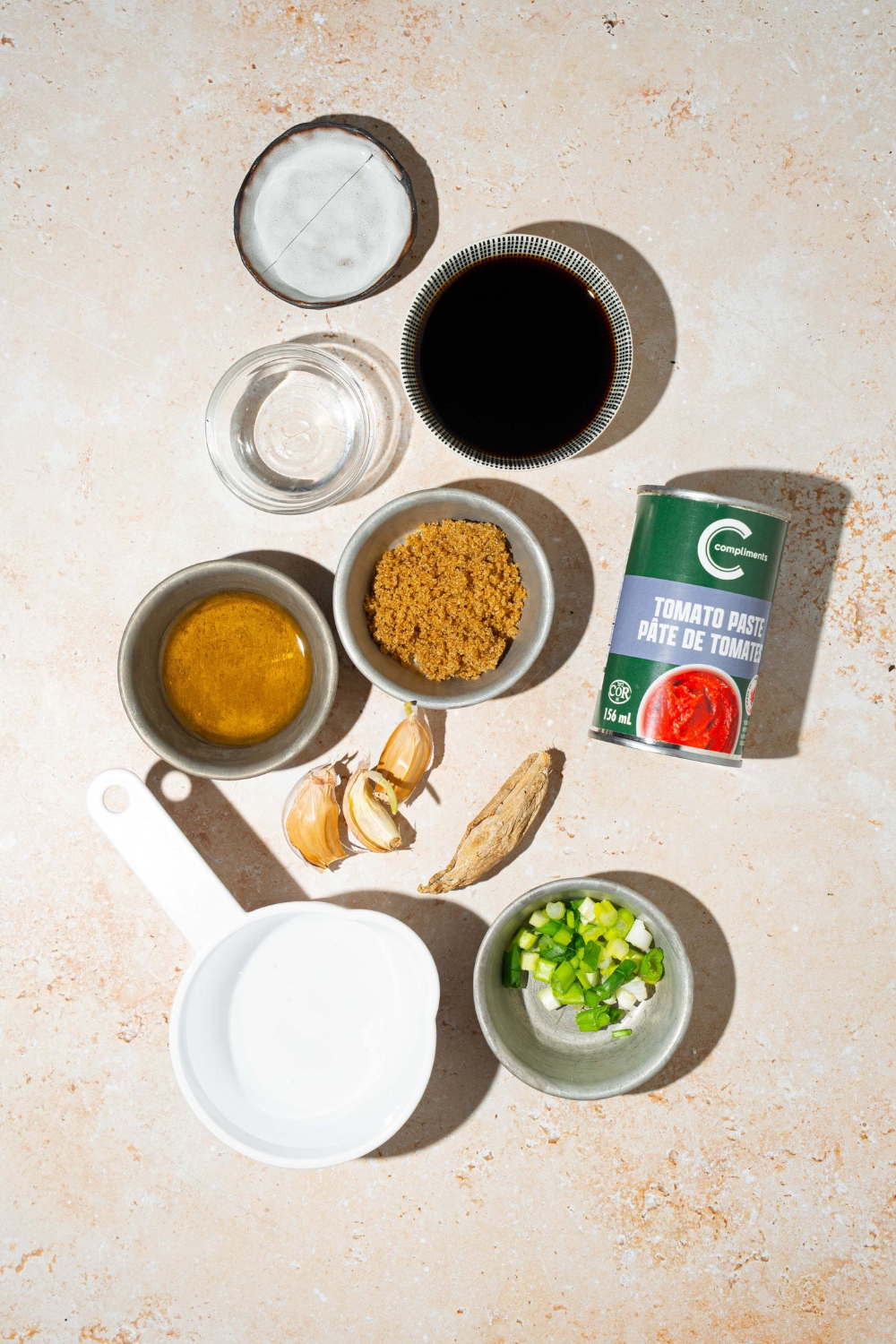 A tan counter with several bowls containing ingredients to make Japanese BBQ sauce including soy sauce, brown sugar, mirin, ginger, garlic, tomato paste, rice vinegar, sesame oil, and water.