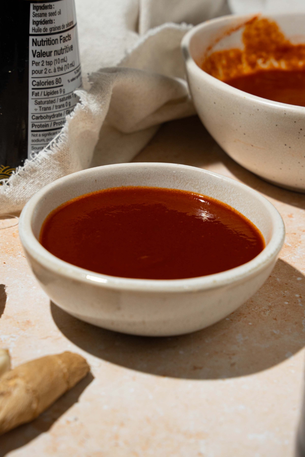 A white bowl with copycat Bachan Japanese BBQ sauce. The bowl is on a tan counter with ginger and a large bowl of sauce.