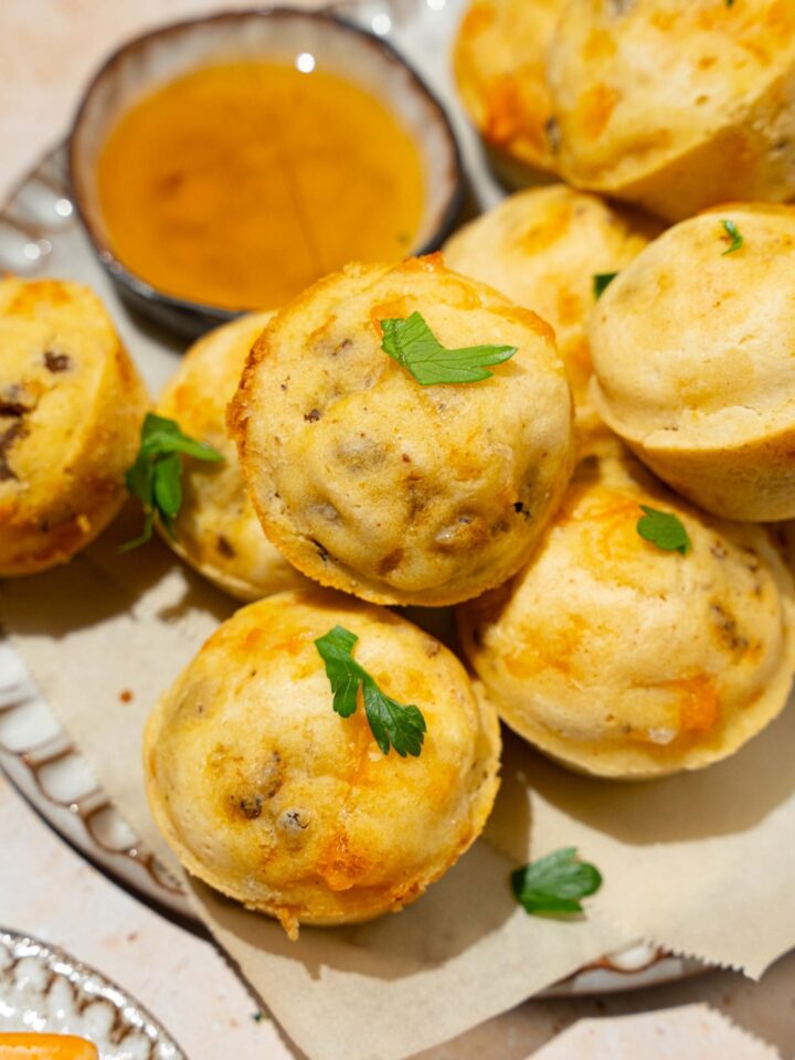 A plate lined with parchment paper with a pile of McGriddle muffins. The plate is garnished with fresh parsley and served with a small bowl of syrup. The plate is on a tan counter.