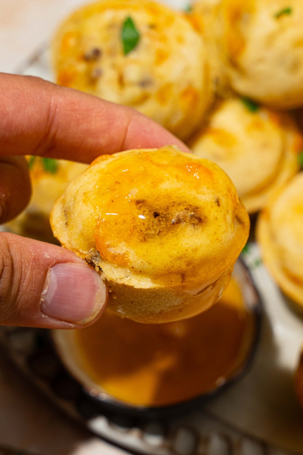 A close up of a hand holding a McGriddle muffin dipped in syrup. There is a plate of muffins blurred in the background.