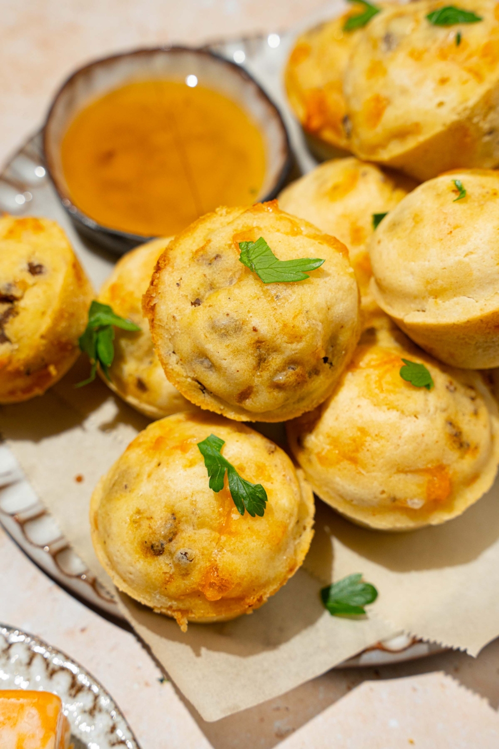 A plate lined with parchment paper with a pile of McGriddle muffins. The plate is garnished with fresh parsley and served with a small bowl of syrup. The plate is on a tan counter.