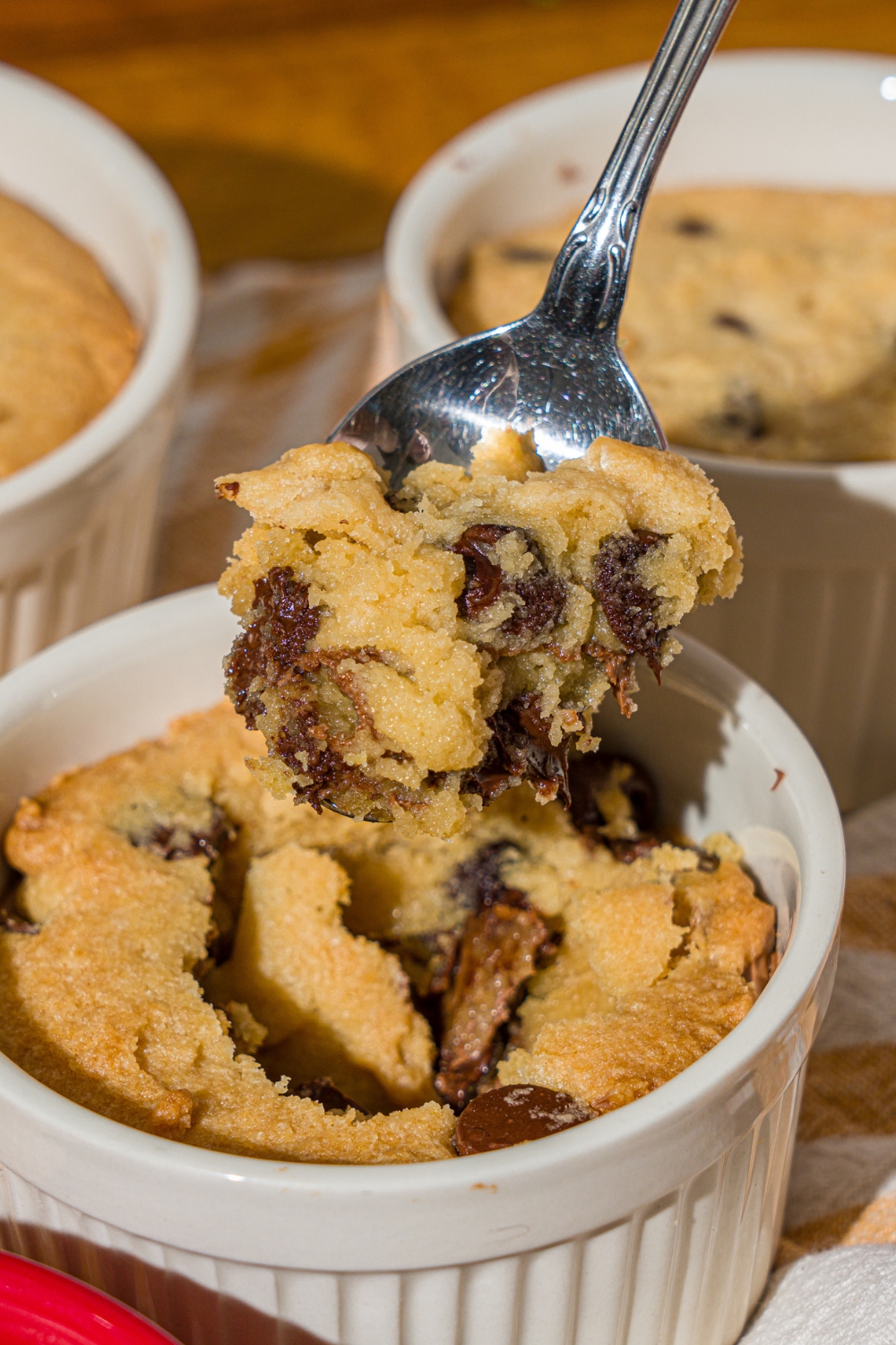 A ramekin with nutella cookie pie with a spoon taking a bite from the pie. The ramekin is on a wooden counter with additional pies.