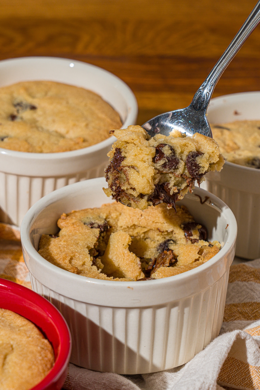 A ramekin with nutella cookie pie with a spoon taking a bite from the pie. The ramekin is on a wooden counter with additional pies.