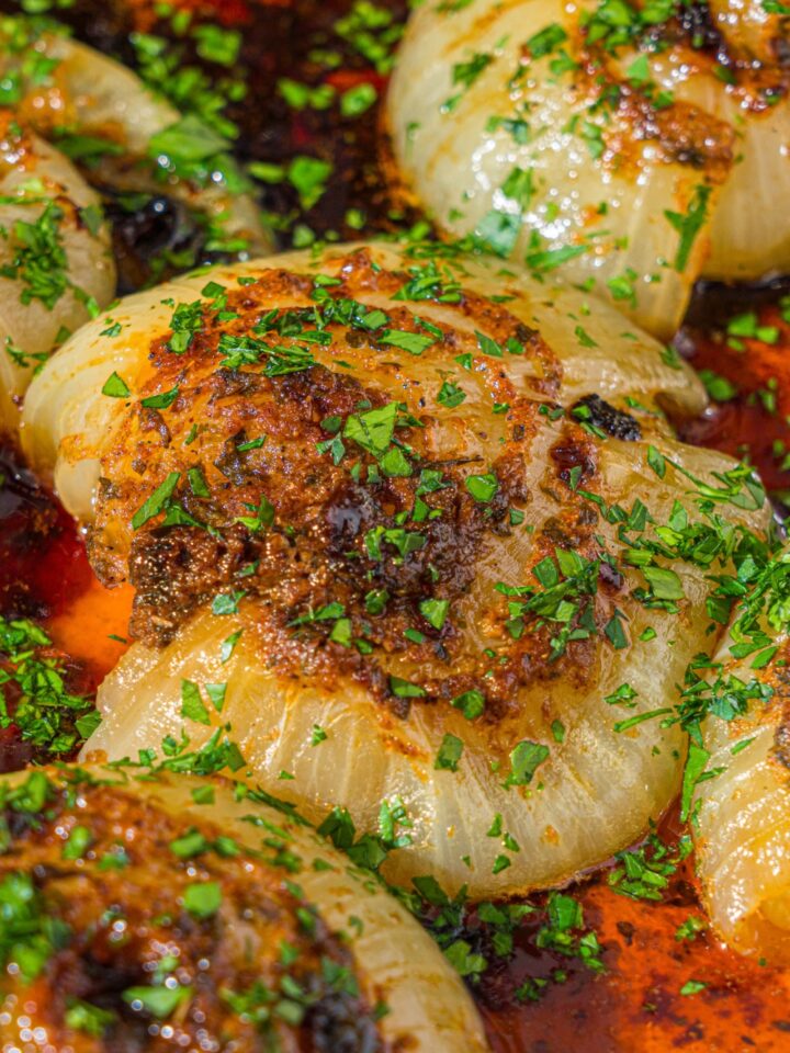 A dutch oven with baked onion boil served in a seasoned butter sauce and garnished with fresh parsley. The dutch oven is on a wooden counter.