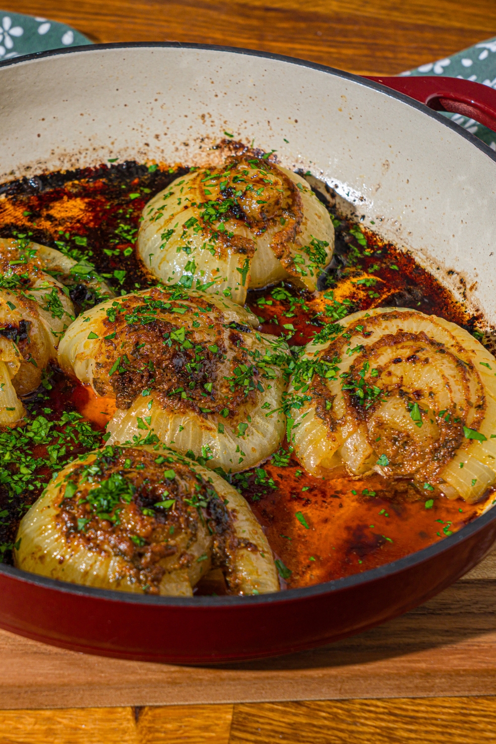 A dutch oven with baked onion boil served in a seasoned butter sauce and garnished with fresh parsley. The dutch oven is on a wooden counter.