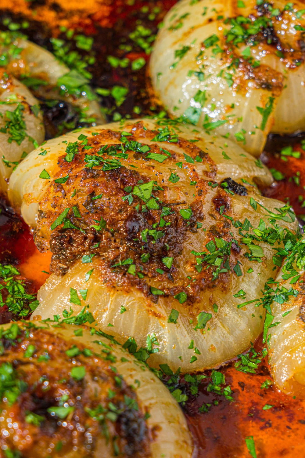 A dutch oven with baked onion boil served in a seasoned butter sauce and garnished with fresh parsley. The dutch oven is on a wooden counter.