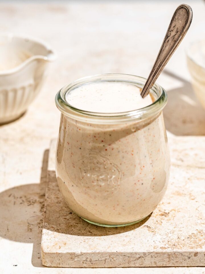 A jar with Outback ranch dressing on a tan counter. There is a spoon in the jar.