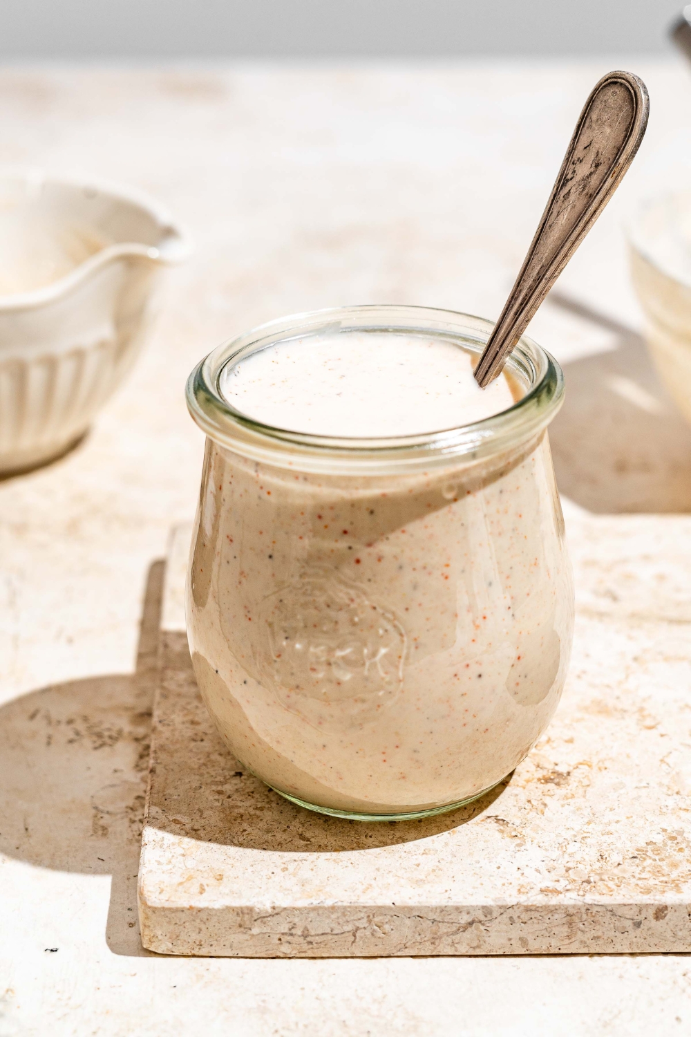 A jar with Outback ranch dressing on a tan counter. There is a spoon in the jar.
