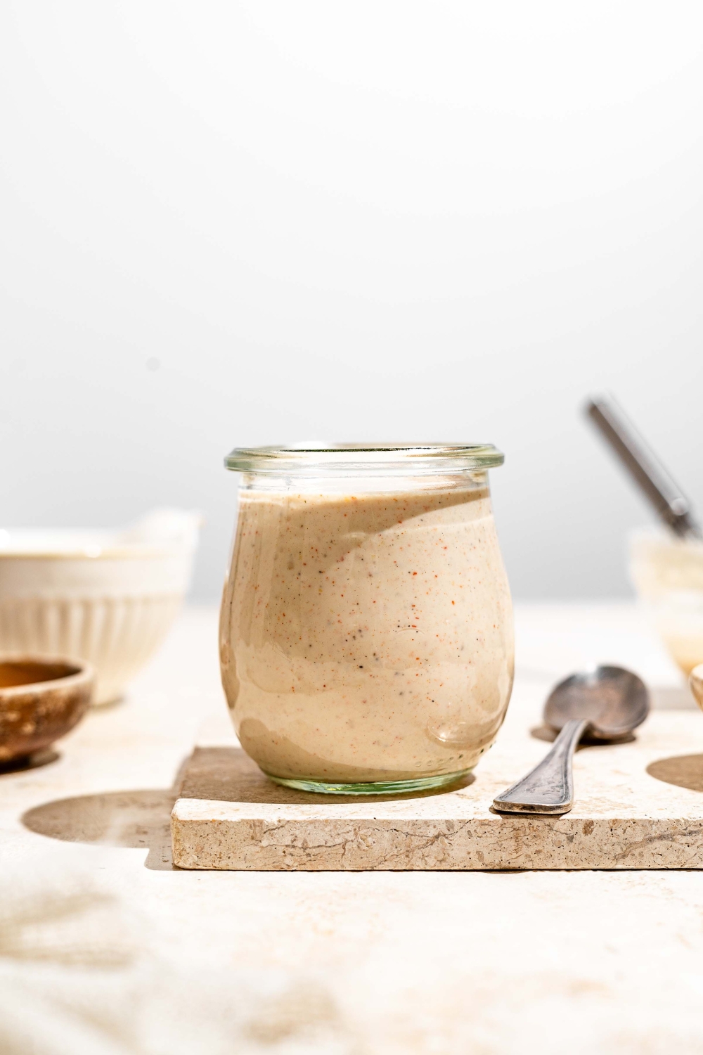 A jar with Outback ranch dressing on a tan counter with a large bowl of dressing and a spoon.