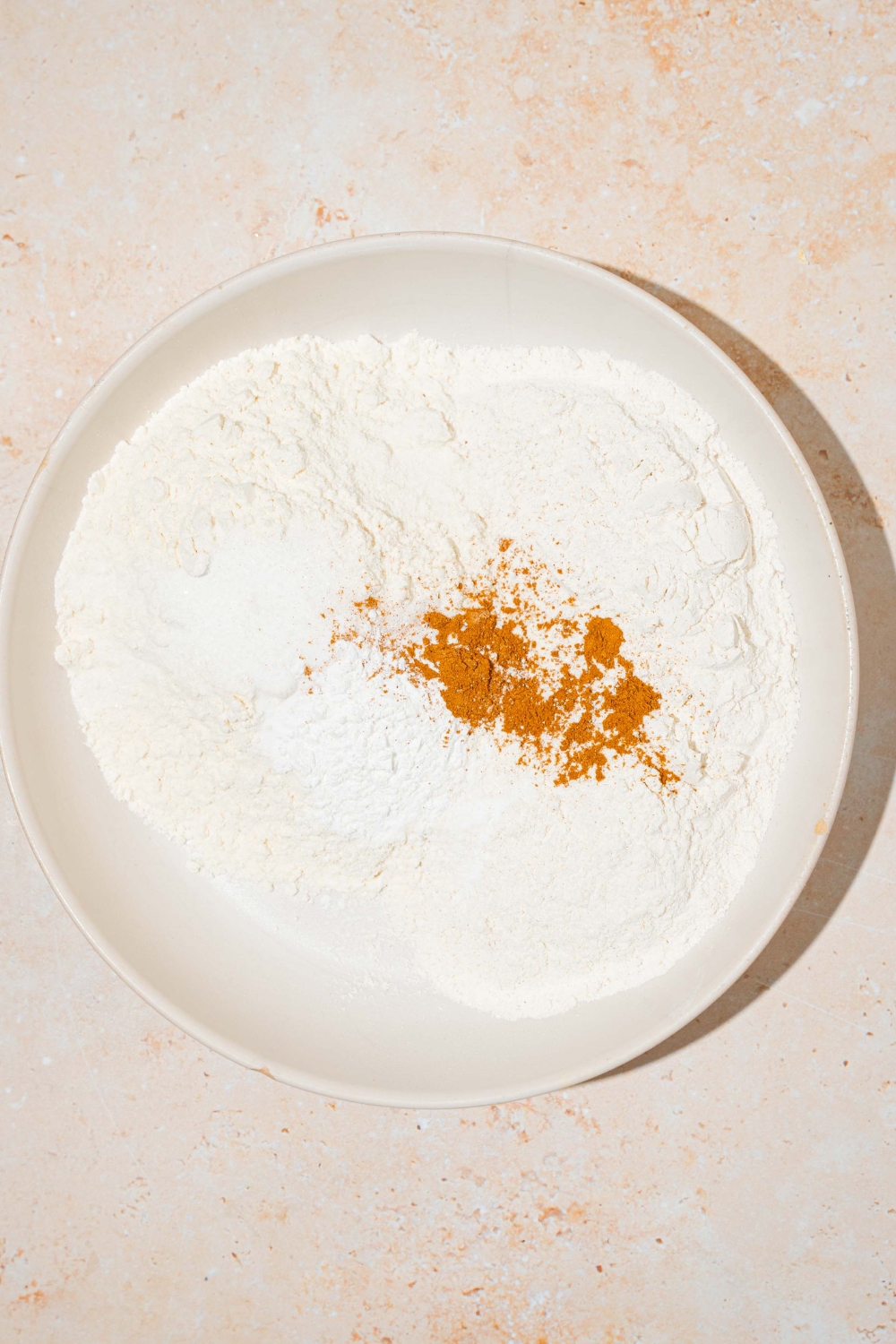 A white bowl filled with flour, baking powder, baking soda, and cinnamon for banana bread.