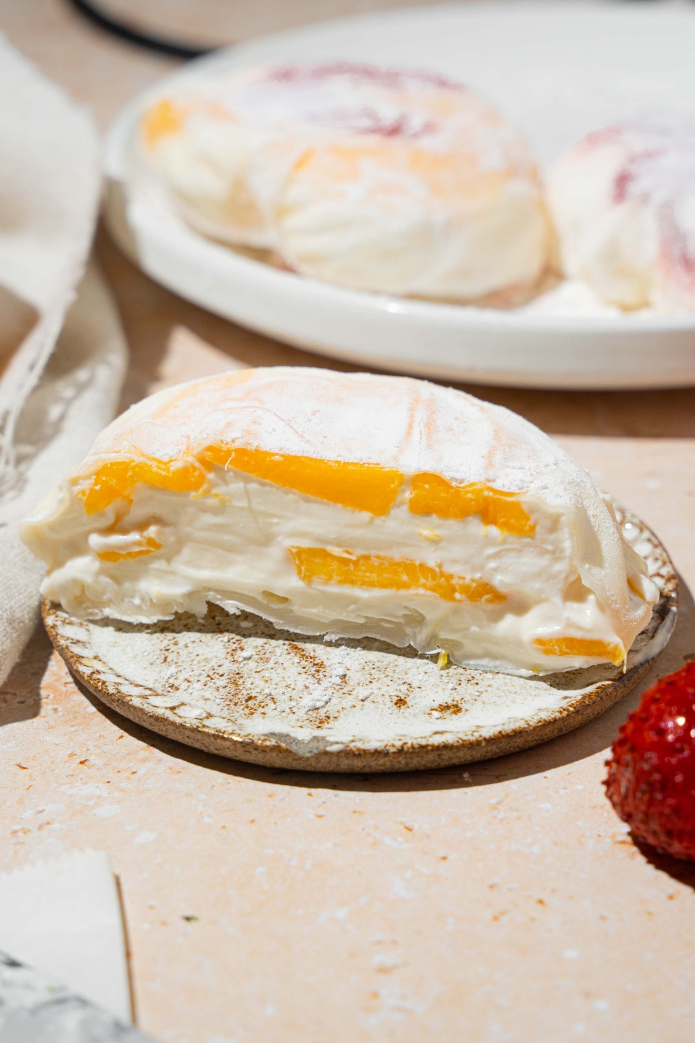 A plate with mango rice paper mochi coated in rice flour and sliced in half. The plate is on a tan counter with an additional plate of mochi.