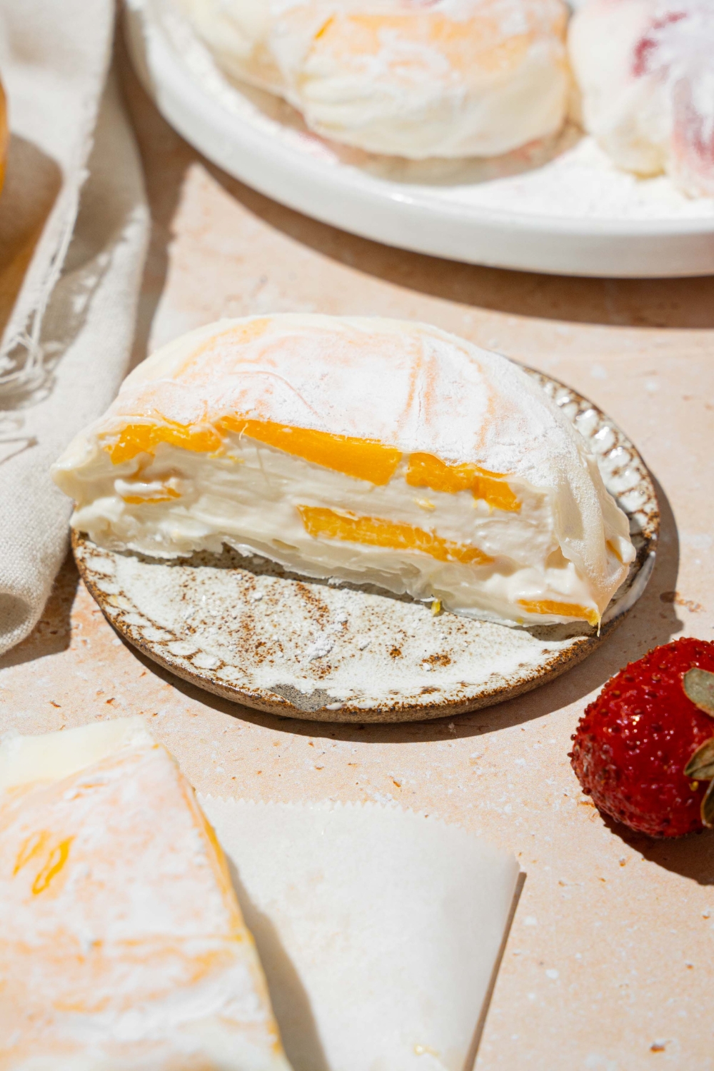 A plate with mango rice paper mochi coated in rice flour and sliced in half. The plate is on a tan counter with an additional plate of mochi.