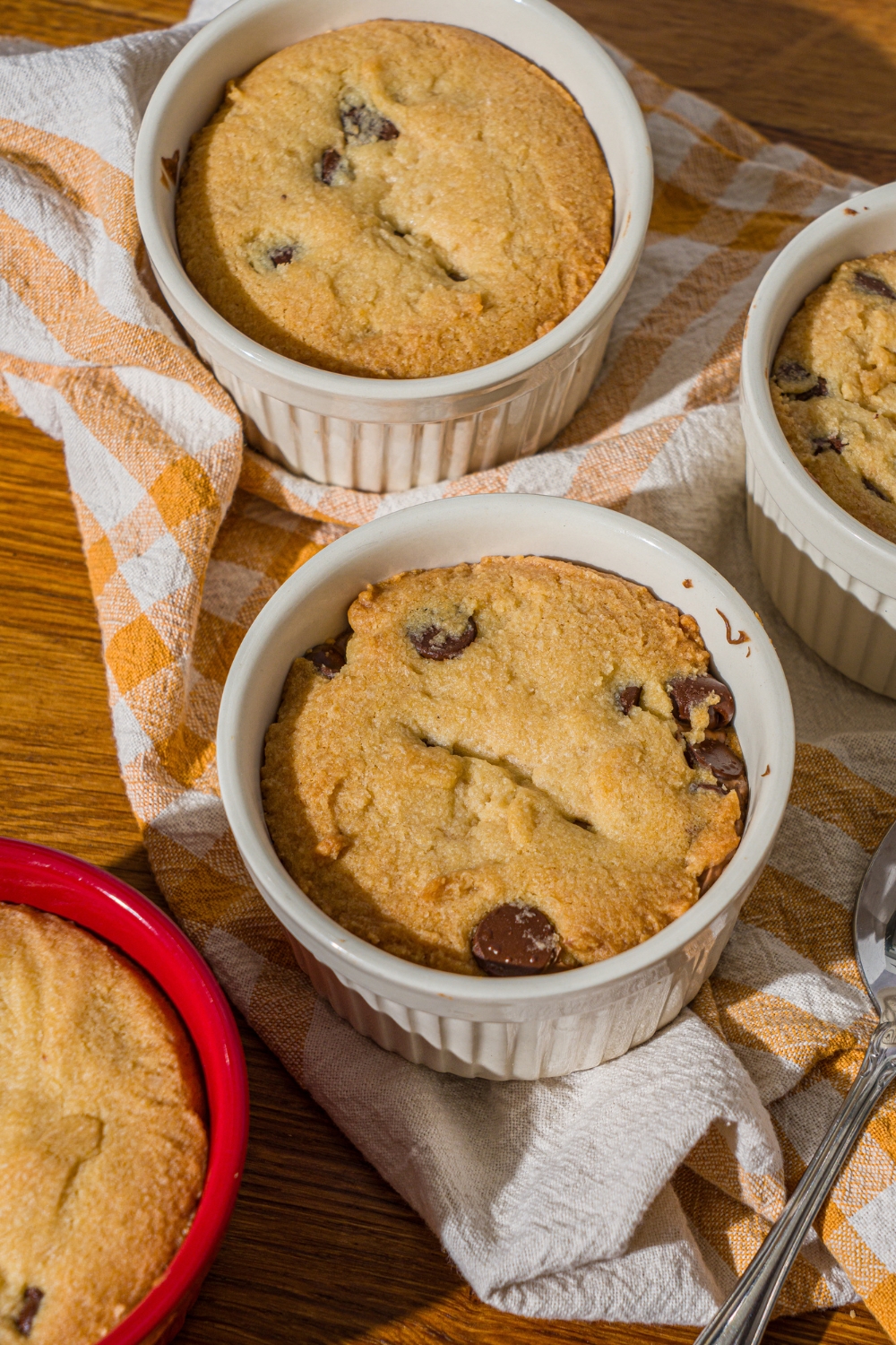 Several ramekins with nutella cookie pie on a wooden counter with a yellow striped napkin.
