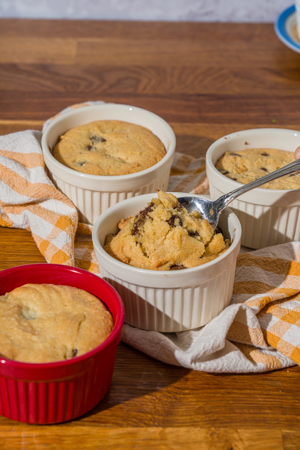 A ramekin with nutella cookie pie with a spoon taking a bite from the pie. The ramekin is on a wooden counter with additional pies and a yellow striped napkin.