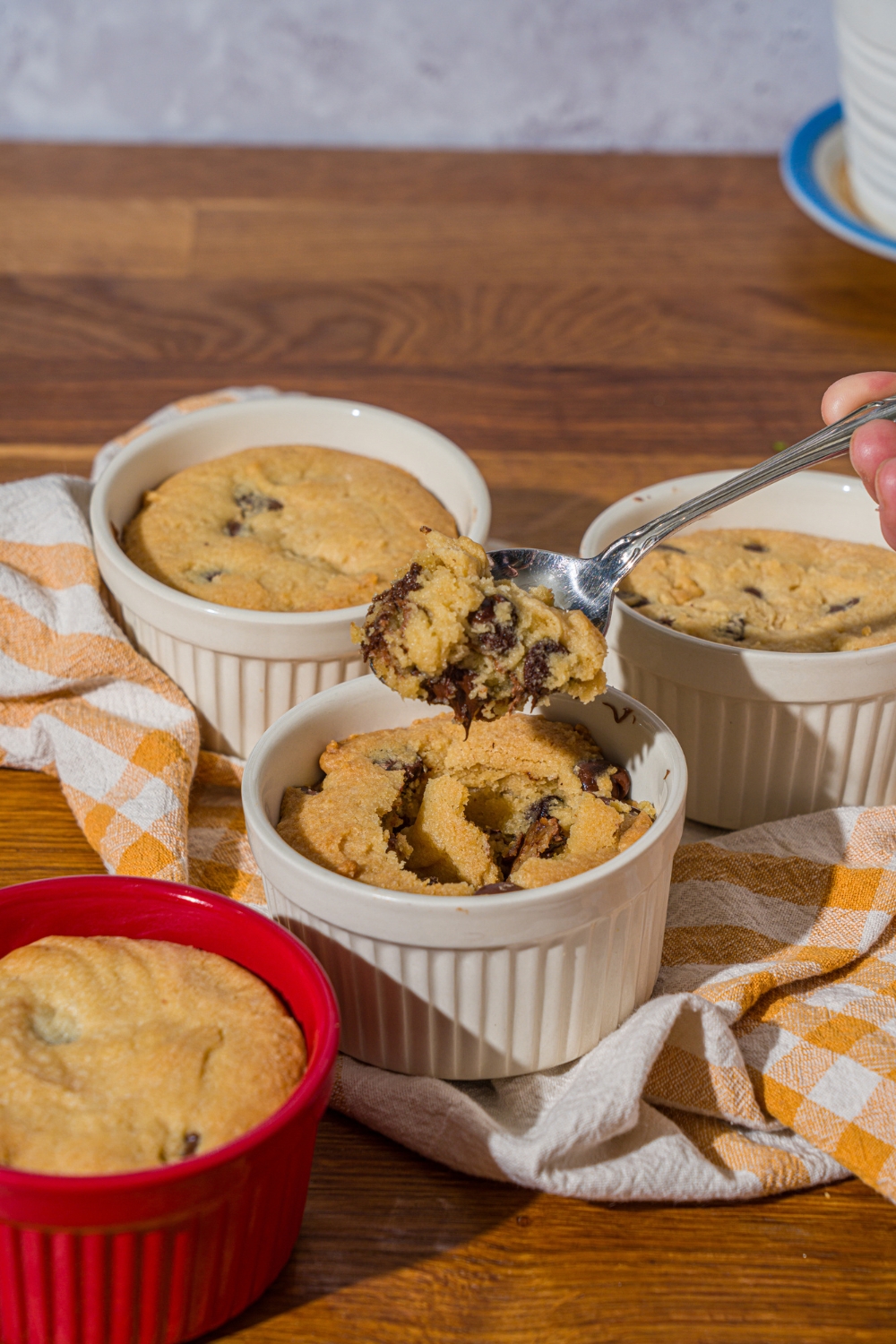 A ramekin with nutella cookie pie with a spoon taking a bite from the pie. The ramekin is on a wooden counter with additional pies and a yellow striped napkin.