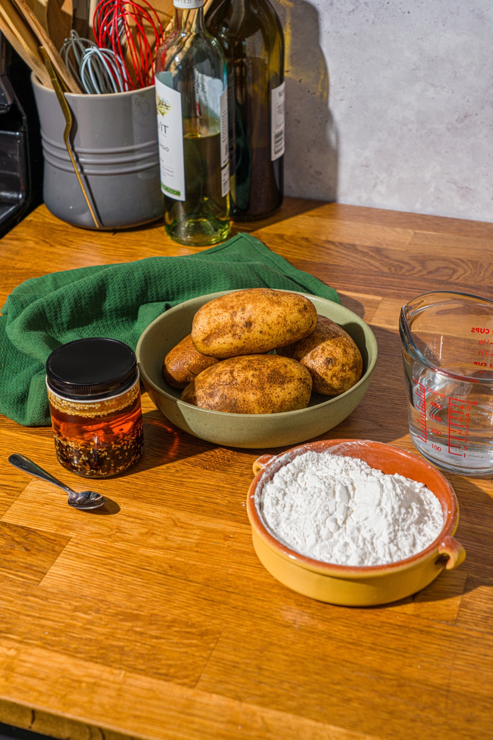 A wooden counter with ingredients to make spicy potato noodles including potato, potato starch, water, and chili crisp.