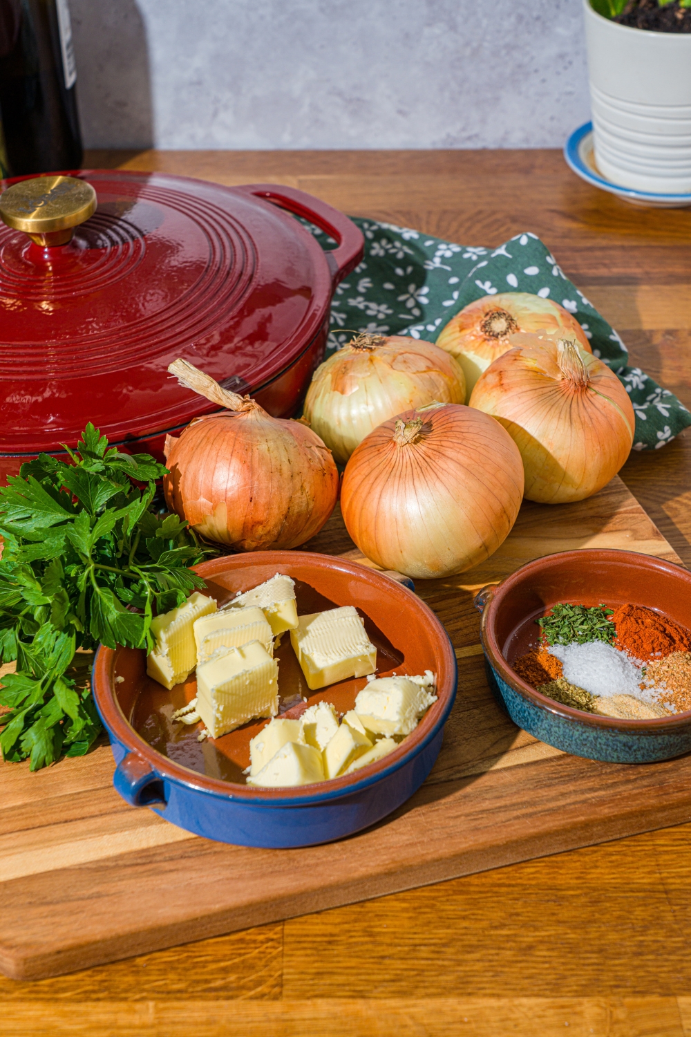 A wooden counter with ingredients to make an onion boil including onions, butter, seasonings, and fresh parsley.