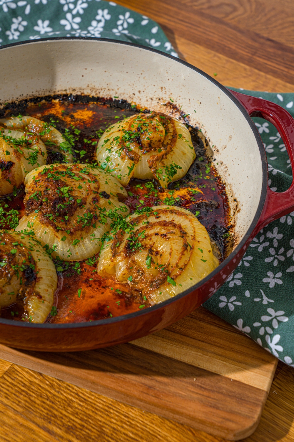 A dutch oven with baked onion boil served in a seasoned butter sauce and garnished with fresh parsley. The dutch oven is on a wooden counter.