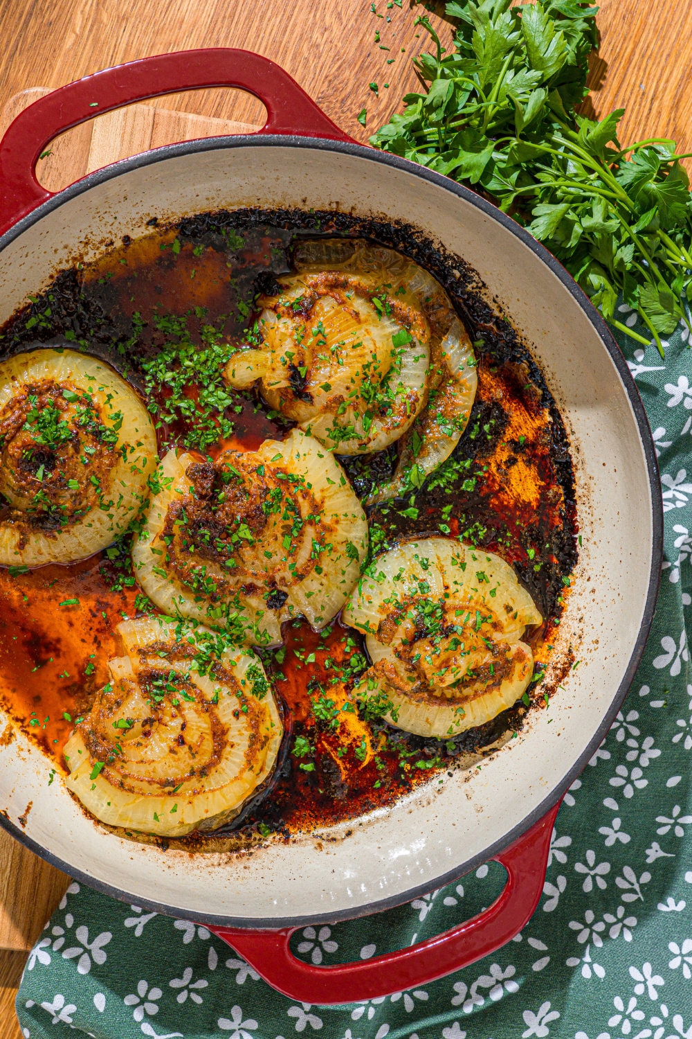 A dutch oven with baked onion boil served in a seasoned butter sauce and garnished with fresh parsley. The dutch oven is on a wooden counter.