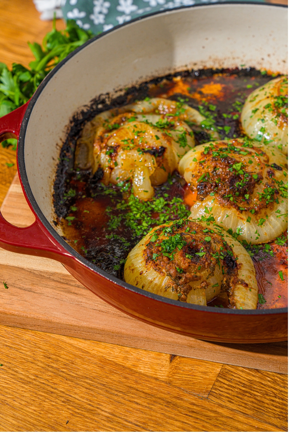 A dutch oven with baked onion boil served in a seasoned butter sauce and garnished with fresh parsley. The dutch oven is on a wooden counter.