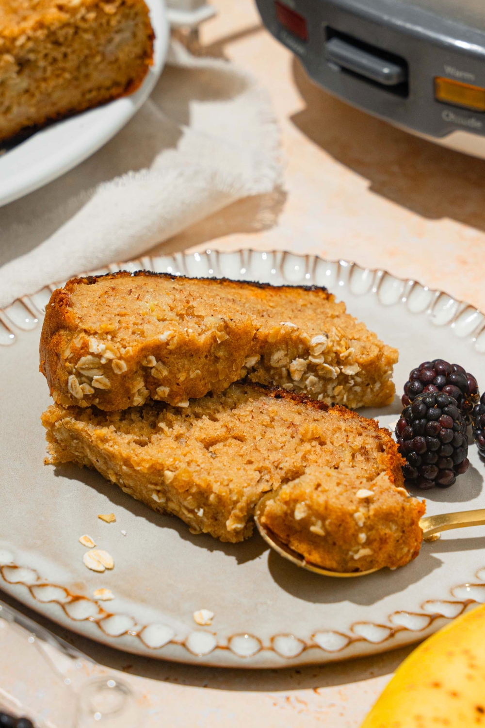 Two slices of rice cooker, banana bread on top of one another with a spoon with a piece of the banana bread on it all on a white plate.