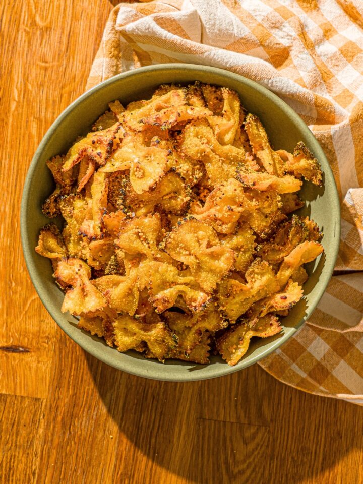Air fryer pasta chips that have mac and cheese seasoning on them in a green bowl on a wood counter.