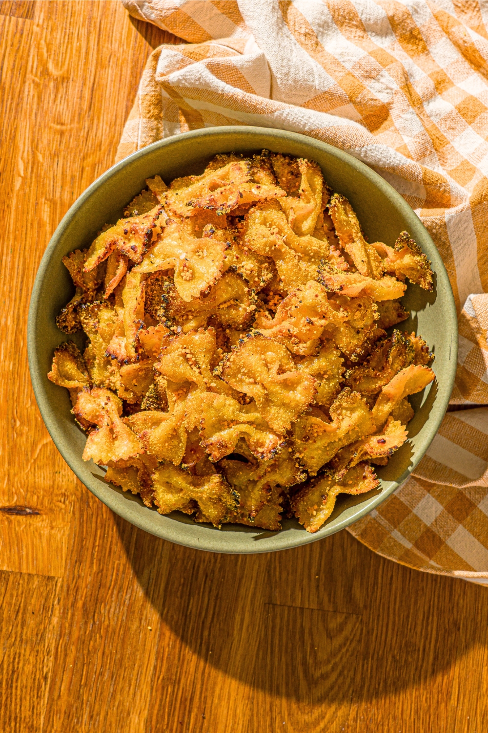 Air fryer pasta chips in a green bowl that is on top of a wood counter with a yellow and white check towel around the front right side of the bowl.