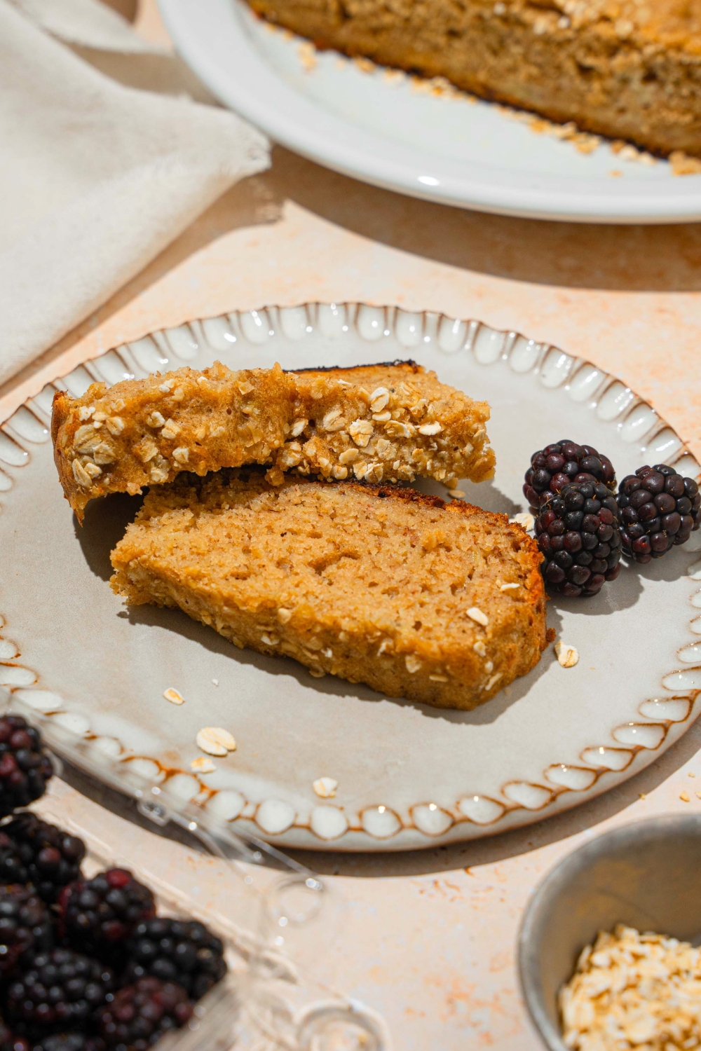 Two slices of rice cooker, banana bread with one leaning on the edge of the other and a few blackberries on a white plate.