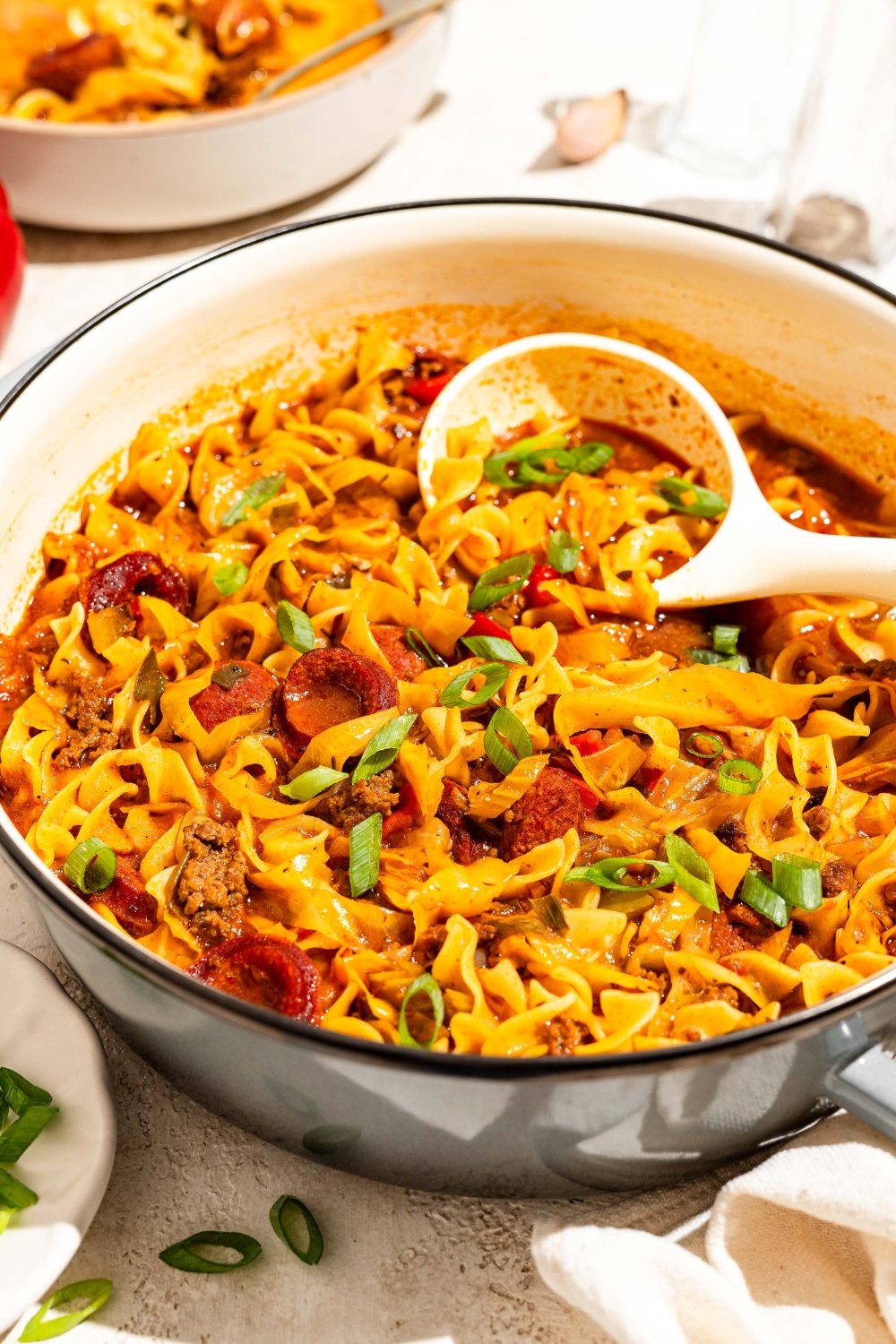 A dutch oven of dirty cabbage and noodles with a ladle taking noodles from the bowl. The dutch oven is on a tan counter.