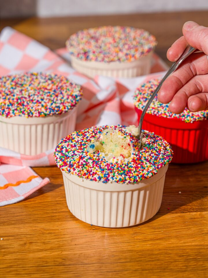 A hand holding a spoon that is submerged into a cake lifting up some of the funfetti cake filling.