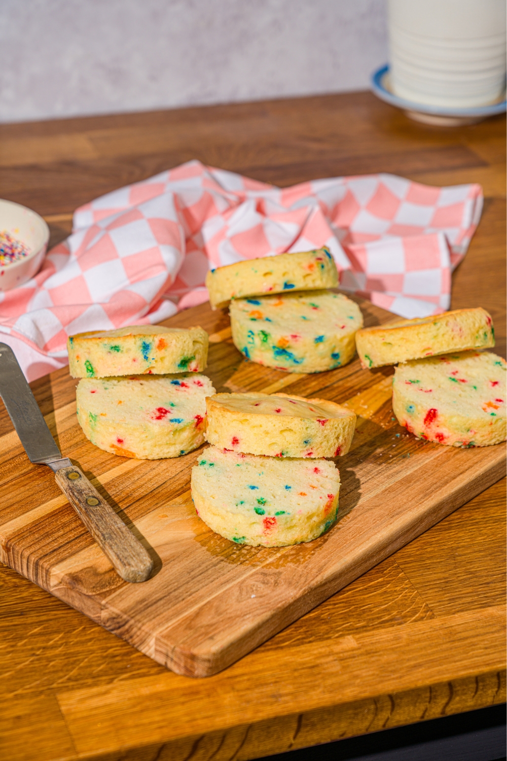 A bunch of sliced circular funfetti cakes on a wooden cutting board.