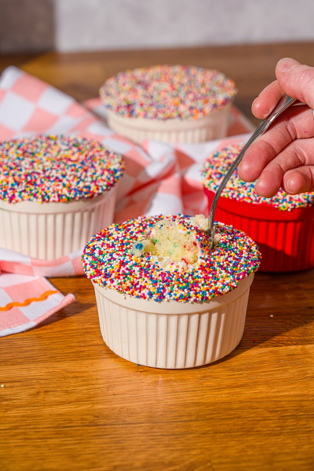 A hand holding a spoon that is submerged into a cake lifting up some of the funfetti cake filling.