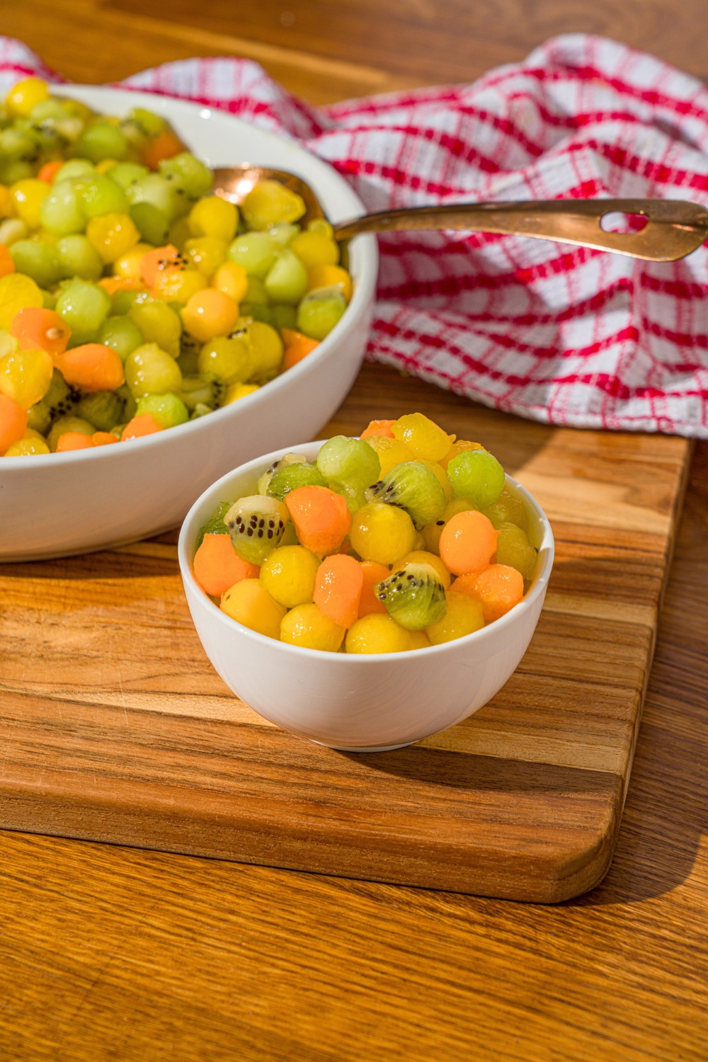 A small white bowl with dot fruit salad in it. Behind that is part of a bigger white bowl with dot fruit salad in it.
