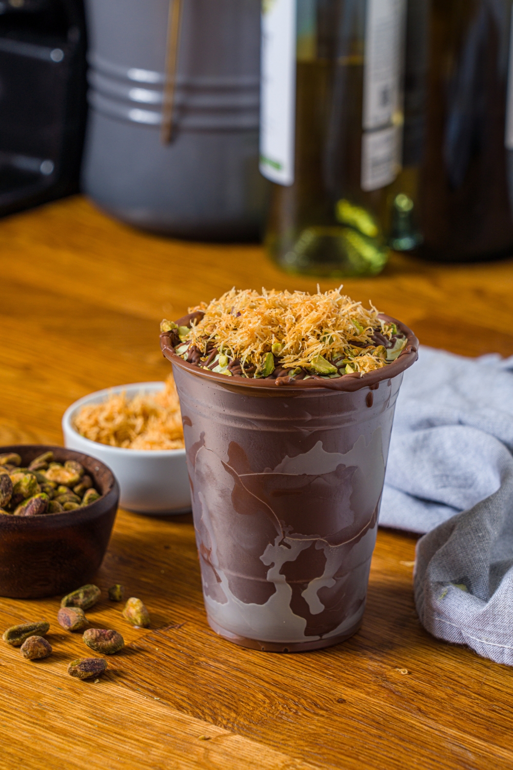 A Dubai chocolate milkshake in a plastic cup that is completely coated in melted chocolate that has been hardened. The shake is on a wooden counter.