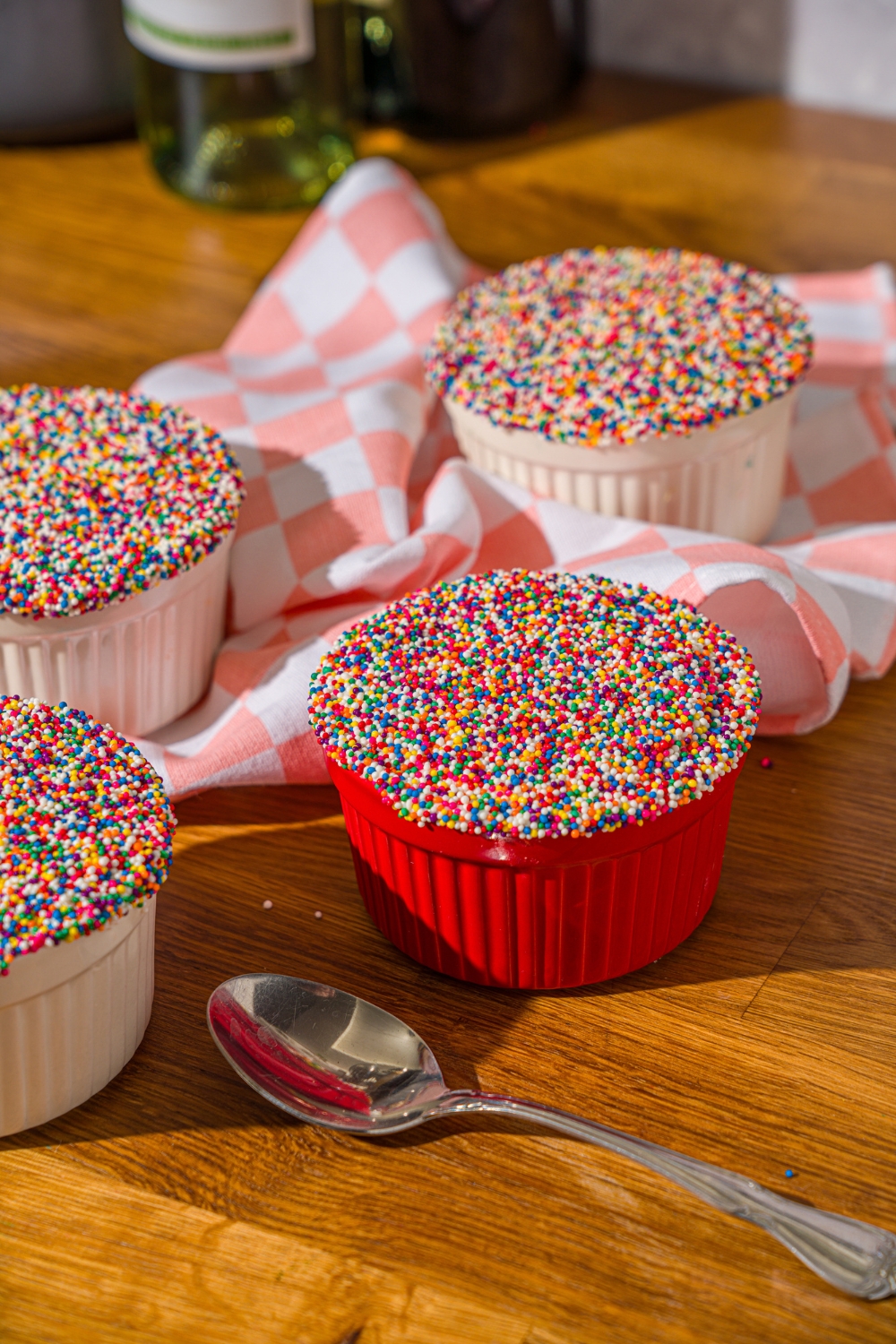 Four dot cakes in individual ramekins on a wooden counter.