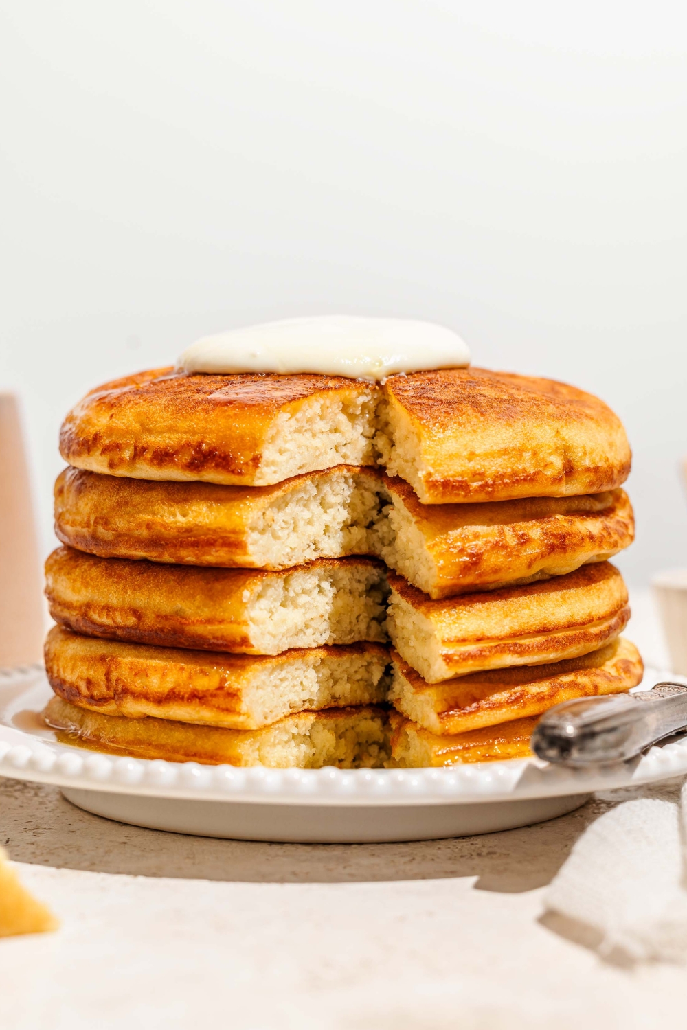 A fluffy stack of four golden diner pancakes on a white plate. The stack has a triangle piece cut out from the front of it so you can see the inside of the pancakes.