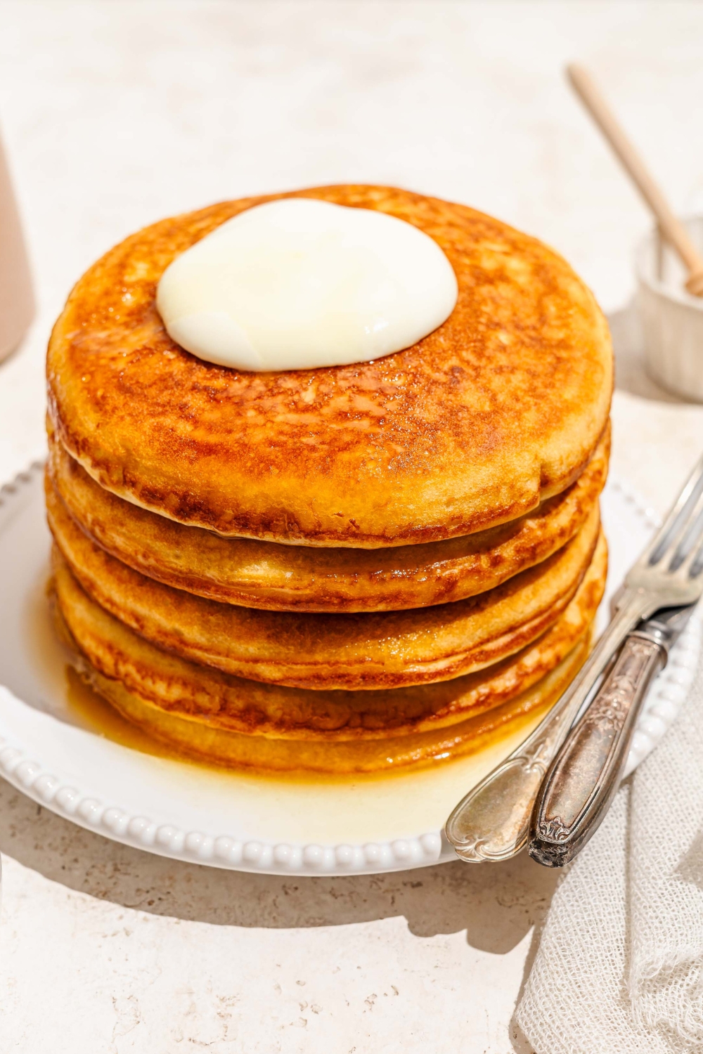 Whipped cream and honey butter on top of four golden diner pancakes on a white plate.