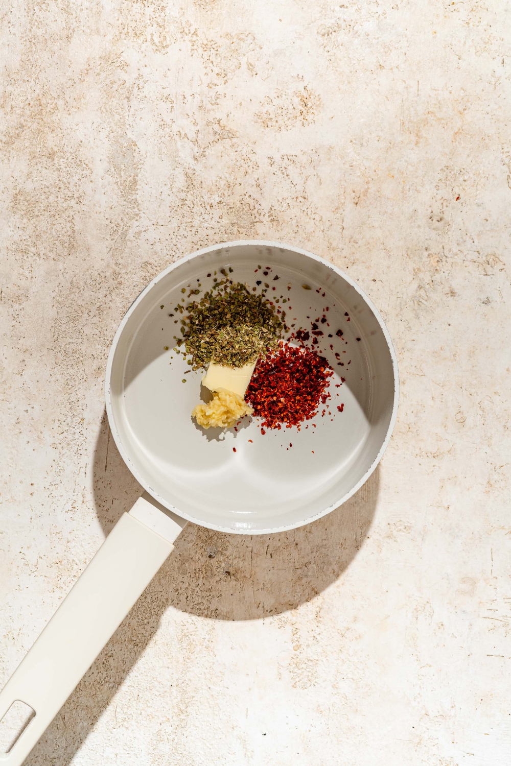 A pot filled with a tablespoon of butter, oregano, red chili flakes, and garlic.