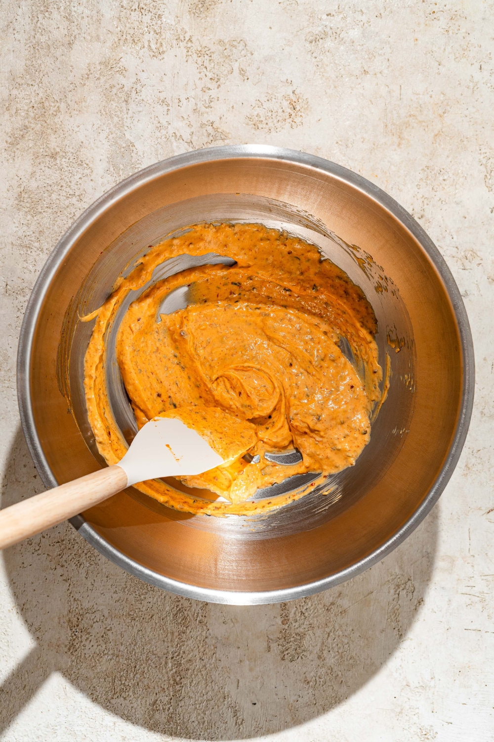 A creamy butter spice mixture in a metal bowl for Peri Peri layers.