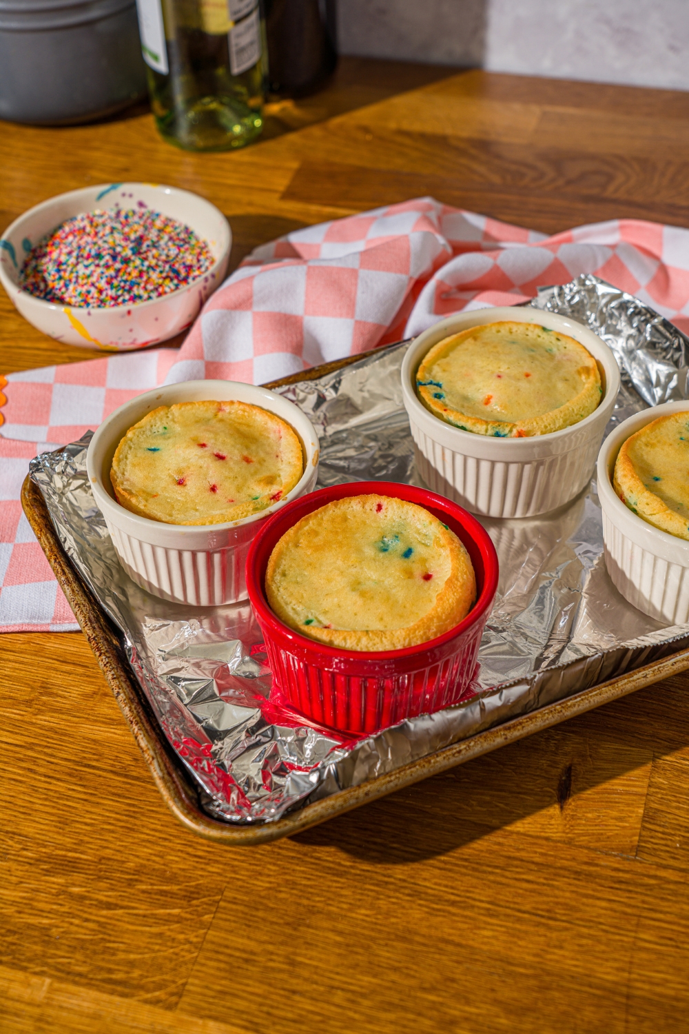 Four ramekins with baked fun Funfetti in them on a foil line baking sheet.