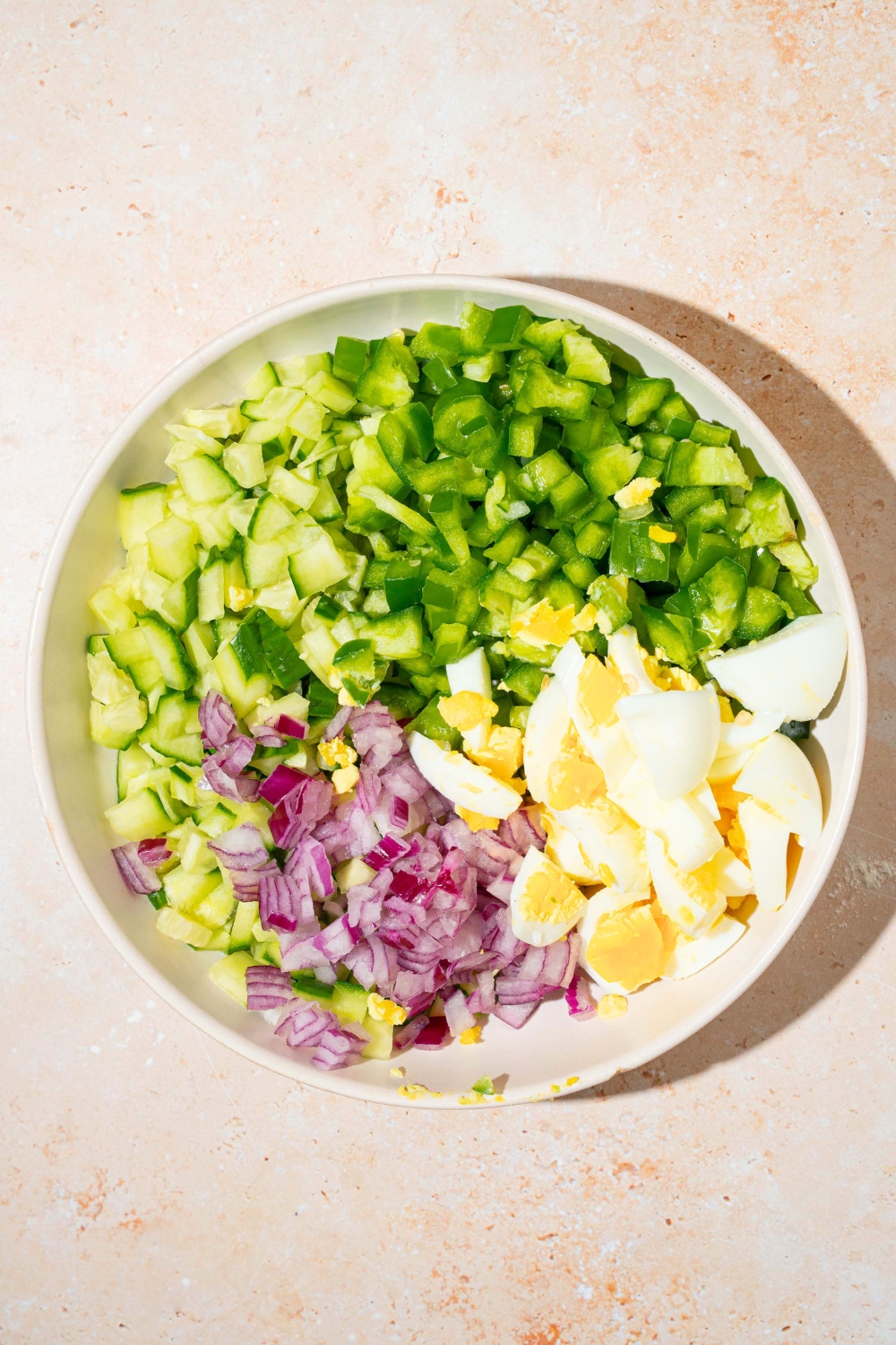 Chopped bell pepper, chopped zucchini, chopped onions, chopped, hard-boiled eggs, in a white bowl.