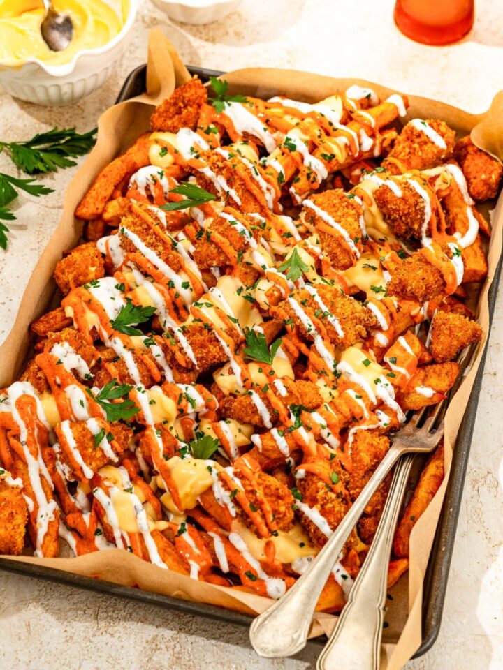 A platter of loaded fries with crispy chicken on top, covered in a cheese sauce, yogurt sauce, and mayo sauce.