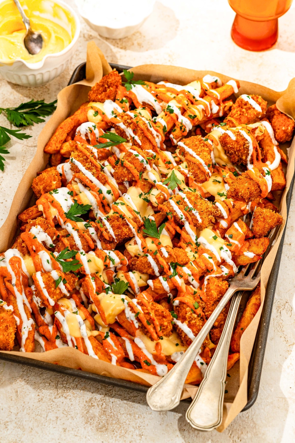 A platter of loaded fries with crispy chicken on top, covered in a cheese sauce, yogurt sauce, and mayo sauce.
