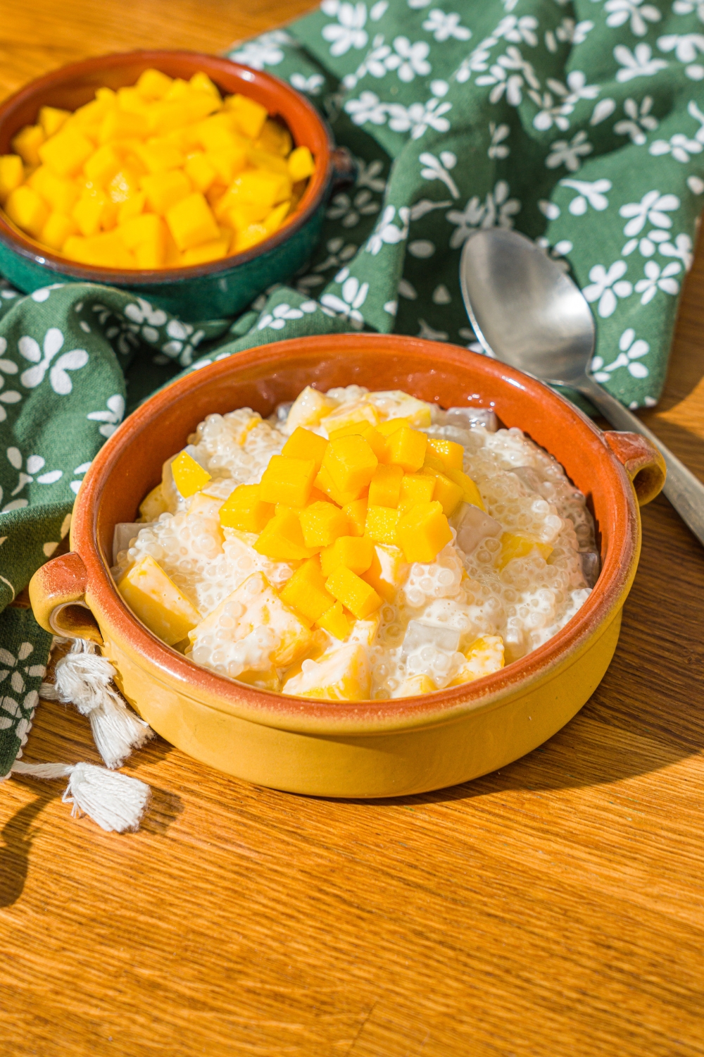 Mango sago in a bowl with diced mango on top. Behind it is a bowl with diced mangos in it.