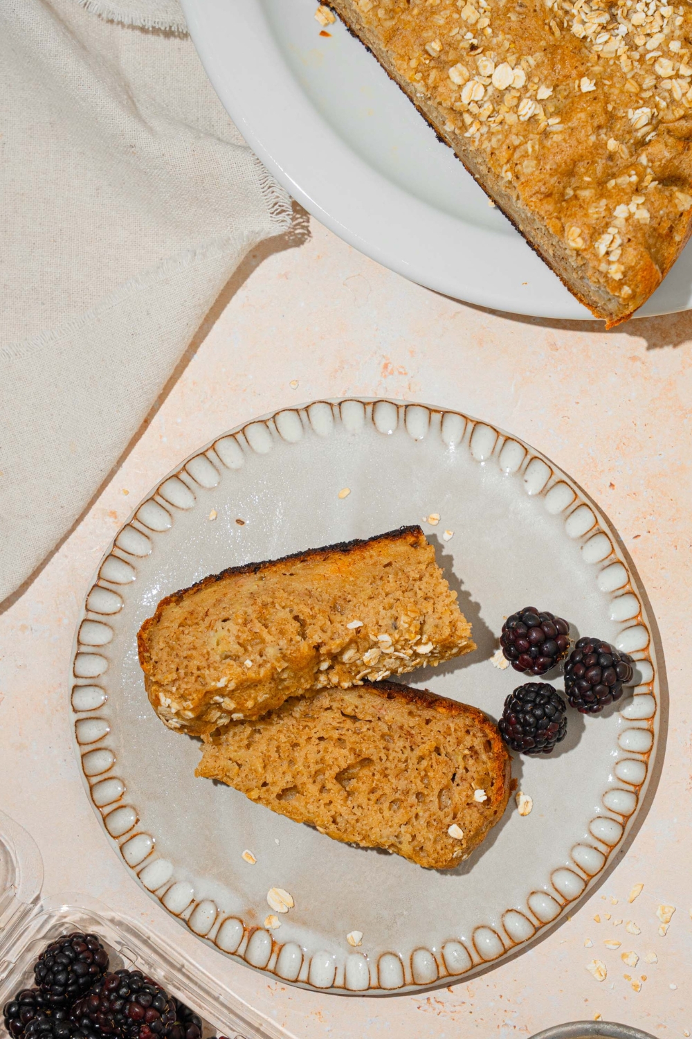 Part of rice cooker, banana bread on a white plate below that is two slices of the rice cooker banana bread on top of a white plate all on a cream counter.