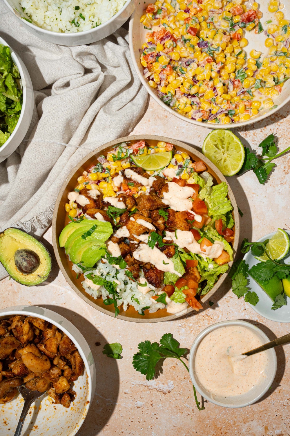 A street corn chicken rice bowl on a white counter. Behind it is the street corn mixture in a bowl and in front of it is the seared cubed chicken in a bowl.
