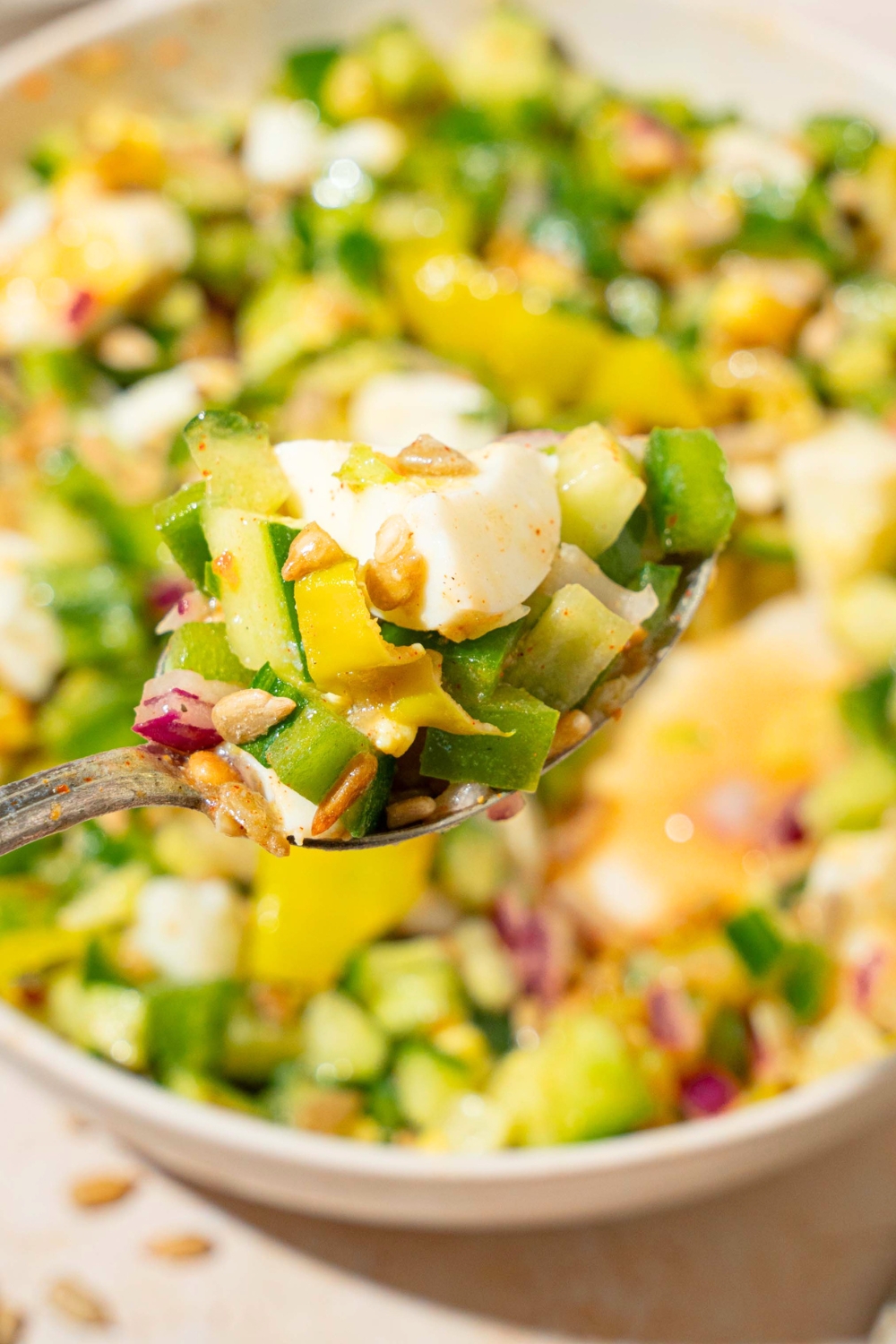 A fork with part of a hard boiled egg, chopped cucumber, green bell pepper, onion, and pepperoncini being held over a bowl filled with the hot girl summer salad.