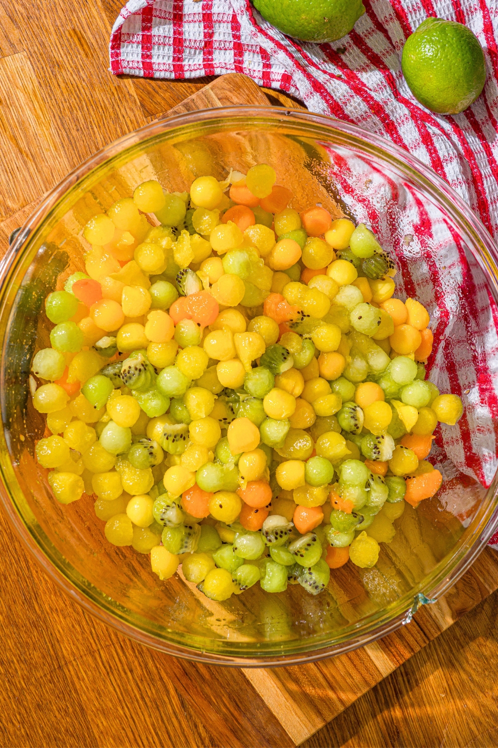 A dot fruit salad consisting of yellow watermelon, honeydew, apricots, and kiwis in a large glass bowl.